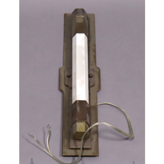 This is a vintage-style wall sconce featuring a sleek, faceted glass tube encased in a geometric brass frame. The design...