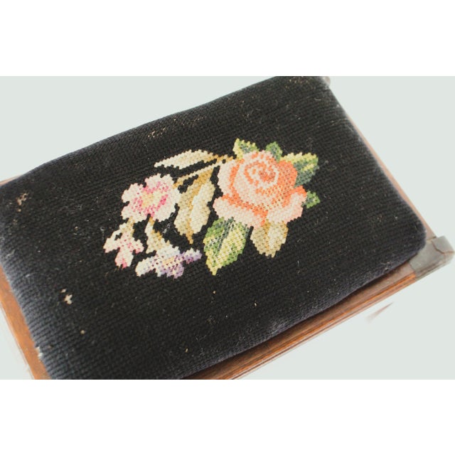 Circa 1890-1910 carved mahogany footstool, featuring a black floral needlepoint cushion top with pink rose embroidery.