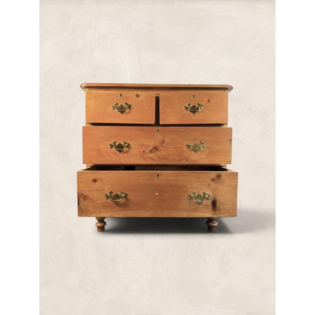 A charming late 19th century English pine chest of drawers featuring a classic two-over-two configuration and turned bun...
