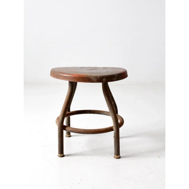 Vintage industrial metal stool with sloped seat and four leg base. Short factory stool featuring sturdy steel construction...