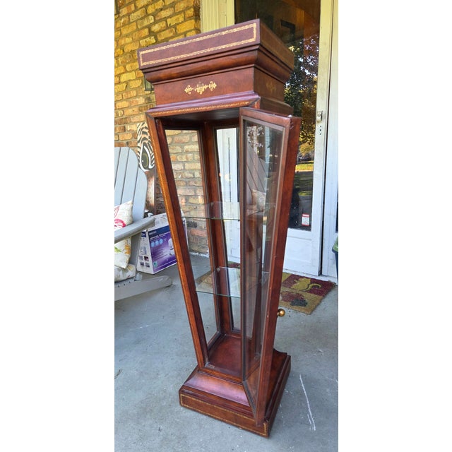 Unique leather wrapped pedestal or curio. Item features clear glass display case base with swing door, two interior glass...