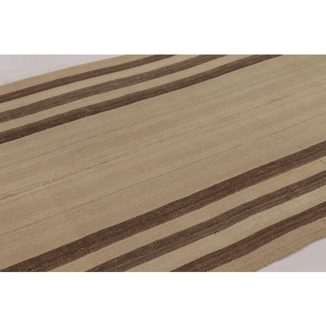 Handwoven in wool, this 5x9 contemporary Rez kilim features a natural beige field framed by rich brown vertical stripes....