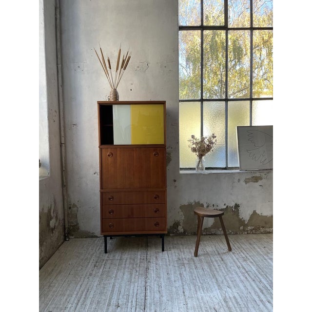 Old storage unit from the 50s with a modernist appearance. with its teak body, its black lacquered metal legs and its two-...