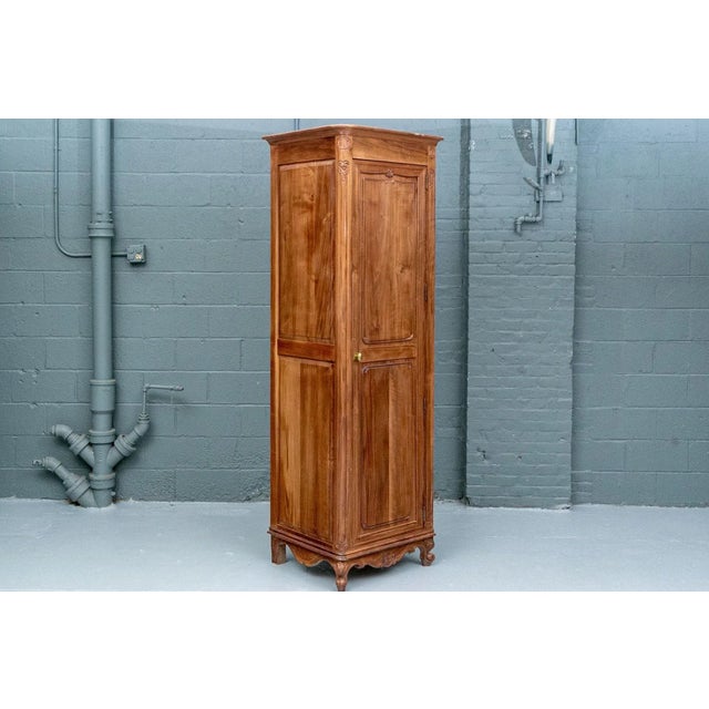 A tall, narrow Louis XV style corner cabinet or chimney cupboard in a warm honey-brown finish with carved floral details,...