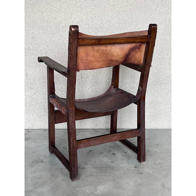 Pair of Spanish colonial style armchairs, having leather both seats and backs, and brass nailheads. Measure: Height to the...