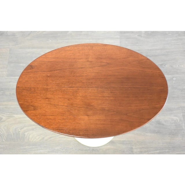 A mid century modern classic tulip end table with an off white matte color pedestal and a walnut oval top designed by Eero...