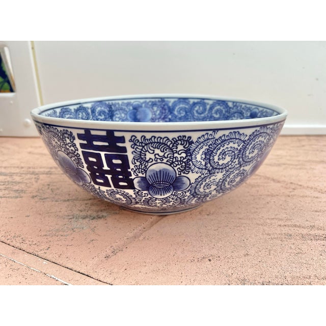 This blue and white ceramic bowl features a double happiness symbol and scrolling floral patterns. Stands 5.5” tall and...
