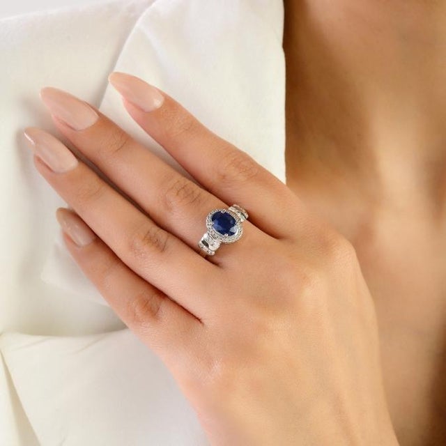 This elegant halo ring features 1 natural oval-cut blue sapphire totaling 1.33 carats, set in 14K white gold. The sapphire...
