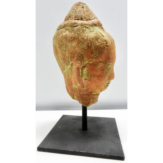 Details speak volumes on this terracotta sculpture of a head that is perched on an iron stand. The natural terracotta...