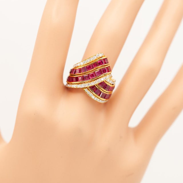 This striking vintage ring features vibrant square-cut rubies channel-set in sinuous diagonal rows, framed by 58 pavé set...