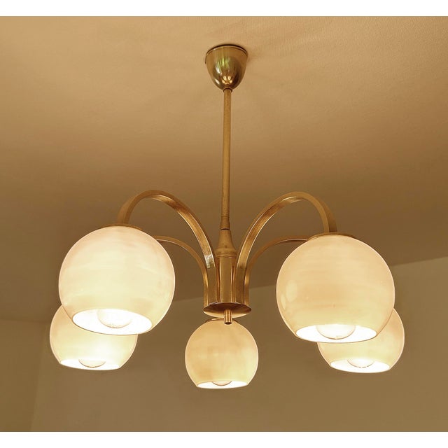 Late Art Deco pendant light from the 1950s featuring a brass structure with 5 curved spokes and ivory color opaline glass...
