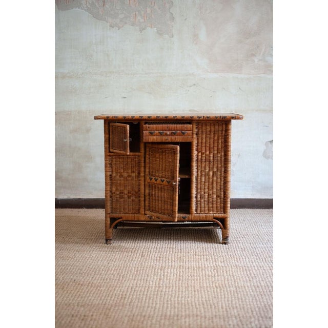Small sideboard crafted in woven wicker, the front featuring a central door, an upper drawer, and a small side cabinet. It...