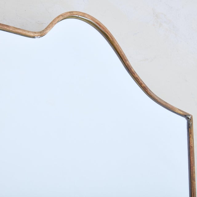 A 1970s Italian shield shaped wall mirror featuring elegant curves along the top and a subtly tapered silhouette. This...