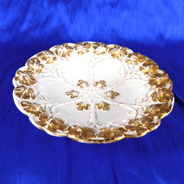 This is a white bowl with a raised relief design of vines, grapes and leaves. The leaves are painted gold, although there...