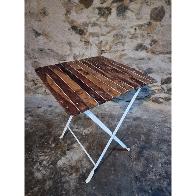 This vintage folding bistro table dates from the 1950s and combines a painted iron base with a walnut wooden slatted top....