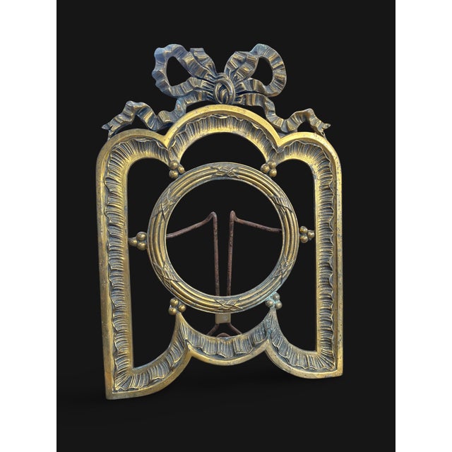 A gilt bronze photograph frame, architecturally designed, adorned with a stylized ribbon bow forming a crown. The mount...