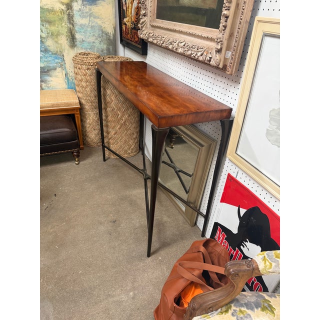 A slim, sculptural console from Theodore Alexander (item 5321-043). A thick, glossy reddish-brown wood top sits on a dark...