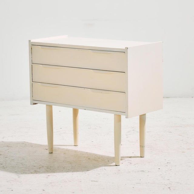 Small white painted dresser or nightstand with special shaped handles and three drawers from the 1960s. The dresser has...