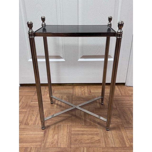 A slim side table in the Directoire style, after Maison Jansen. The frame is polished nickel, with column legs topped by...