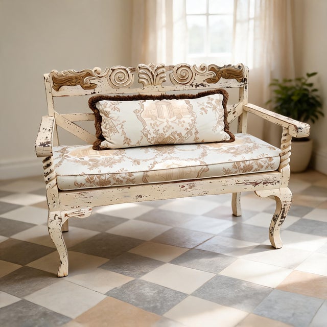 A charming vintage French Country style carved wood settee featuring a distressed cream painted finish, custom toile...
