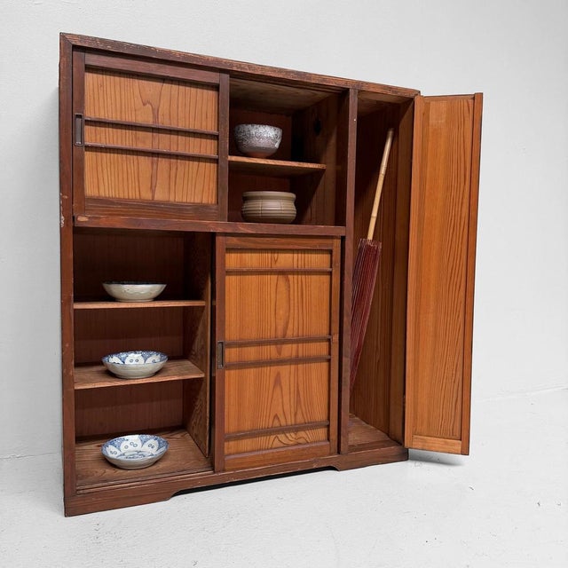 A Japanese storage cabinet with sliding doors, a tall side compartment and a warm contrast between darker and lighter...