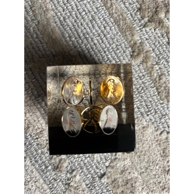 A whimsical 2" square lucite cube with bright floating pennies, all dated 1972, mounted on a black base with tiny bun...