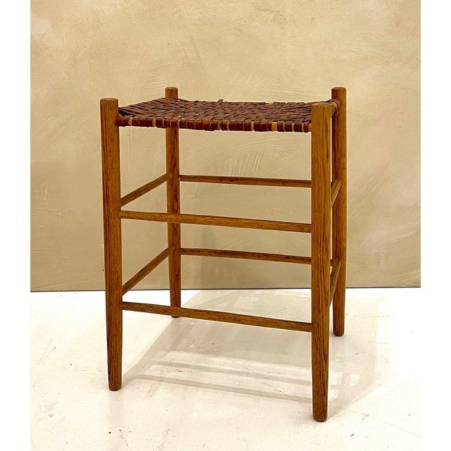 Vintage woven leather stool with a solid oak frame, featuring a handwoven strap seat and clean, architectural lines. The...