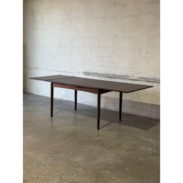 This exceptional expandable dining table features a clean rectangular top supported by slender tapered legs. Two...