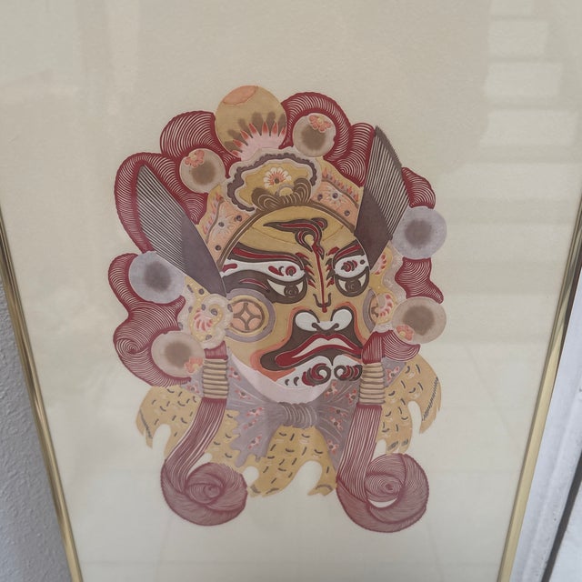This framed vertical art piece features a trio of traditional Chinese theatrical and ceremonial face-paint or mask motifs,...