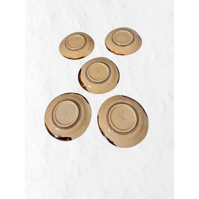 A quietly sculptural set of five Japanese studio pottery plates, each hand-thrown in warm, sandy-toned stoneware and...