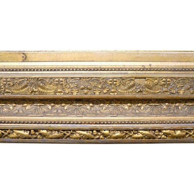 This antique wall mirror features a rectangular form with a richly detailed gilt wood frame. The frame is adorned with...