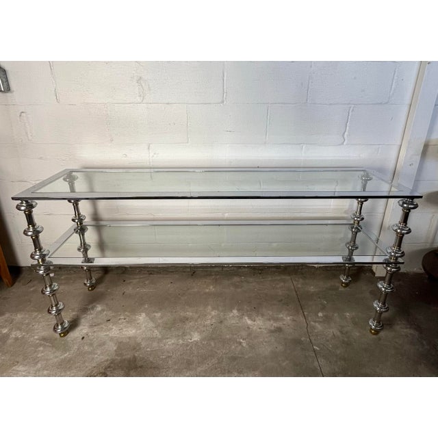 This elegant piece is a Mid-Century Modern two-tier console table, often attributed to the high-end French design firm...