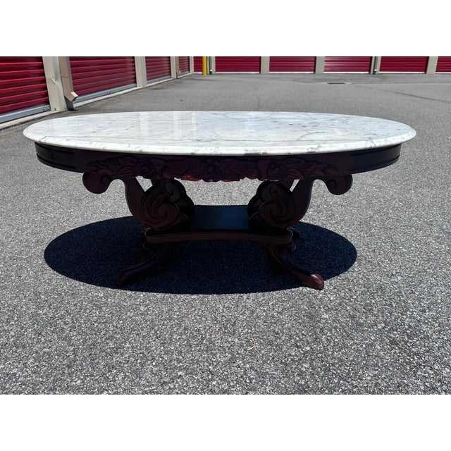 An elegant vintage Victorian Revival center table featuring a substantial oval white marble top resting on an ornately...