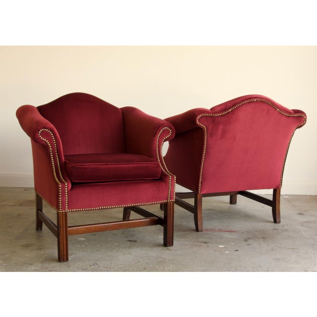 A handsome pair of Chippendale-style club chairs with a graceful camelback silhouette and generously scrolled, rolled...