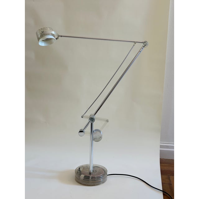 Fully articulated task lamp in polished chrome with acrylic counterweight system and transparent disc base. The scissor-...