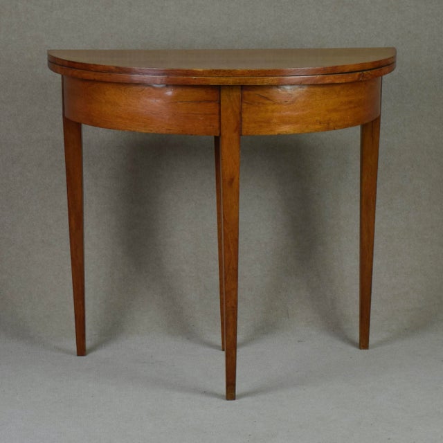 Neat card table in light Mahogany and all parts in original. Demi lune form. Foldable top with extendable middle back leg.