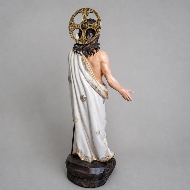 The Risen Christ stands with an open, welcoming gesture, wearing a flowing white drape and holding a Resurrection banner....