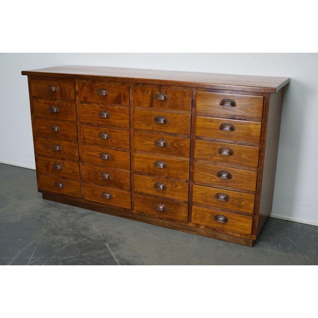 This apothecary cabinet was made circa 1950s in Germany. It features 24 drawers with metal cup handles. It remains in a...