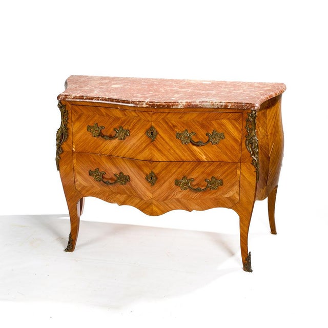 A Louis XV style bombé commode from the late 19th century, veneered in wood with a red marble top and rich bronze...