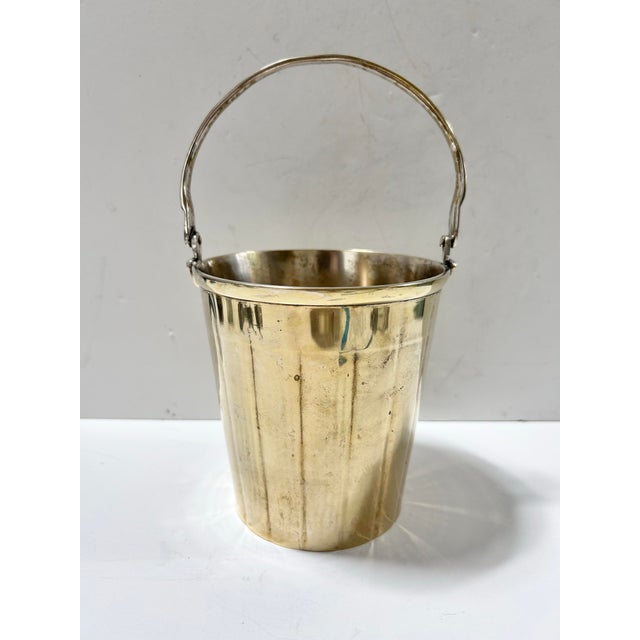 A petite vintage ice bucket crafted from silverplated brass, with a streamlined cylindrical body and hinged swing handle....