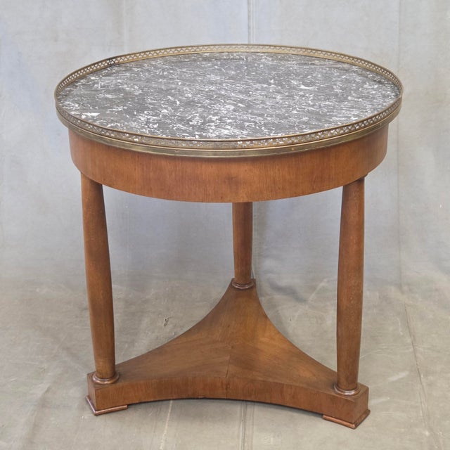 A classic antique 1930s French empire cherry wood guéridon table with inset black marble top surrounded by a pierced brass...