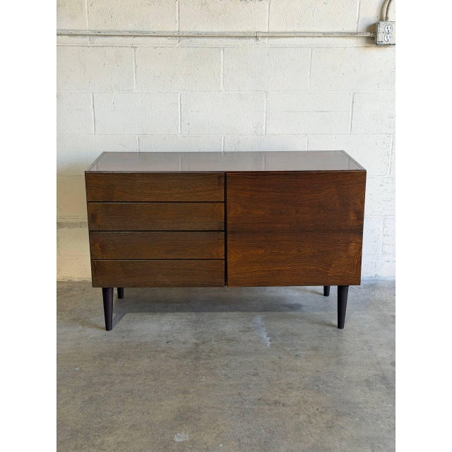 This dark rosewood sideboard pairs four stacked drawers with a full-height cabinet door. A clean rectangular case, handle-...