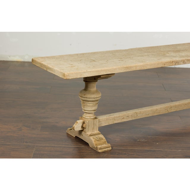 A French bleached walnut bench from the 19th century with trestle base made of two turned baluster legs connected to one...