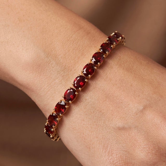 A classic tennis bracelet featuring a continuous row of rich, deep-red oval garnets set in a warm gold-tone sterling...