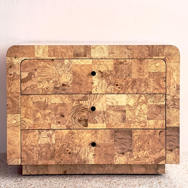 This dresser features a striking modern silhouette wrapped in faux burl wood laminate veneer, known for its unique,...