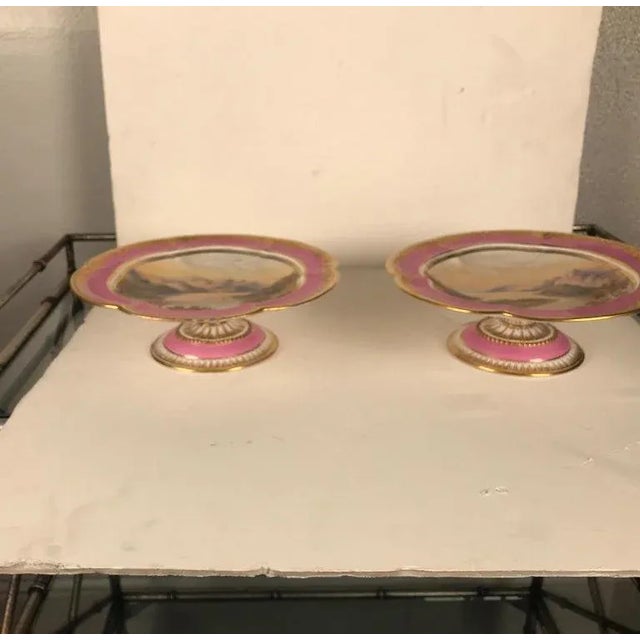 A pair of antique English hand painted and raised gilt porcelain compotes. Each one is painted a different Irish seaside...