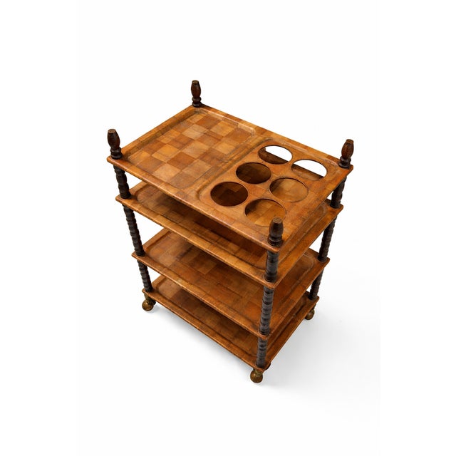 Serving trolley with four pressed wood trays and a turned solid wood frame, probably teak, on four wheels. It shows some...