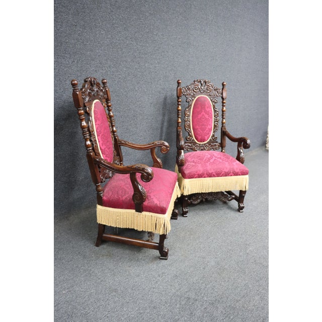 A pair of Jacobean Renaissance style throne chairs in Walnut with stretcher base and tassel trim.