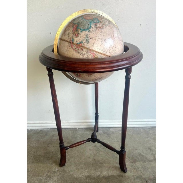 Vintage globe mounted on a mahogany wooden stand with three elegantly turned legs. A brass colored meridian ring encircles...