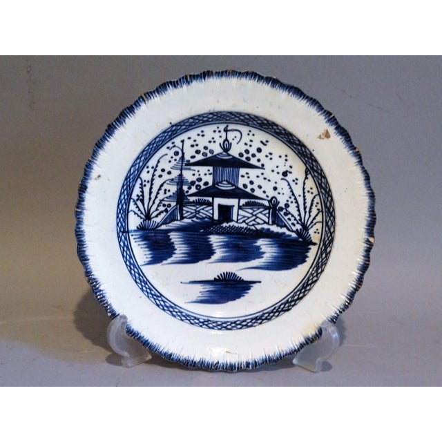 A circa 1790, English pearl ware wall plate with a fluted feathered edge surrounding a Chinese pagoda and garden. It is...